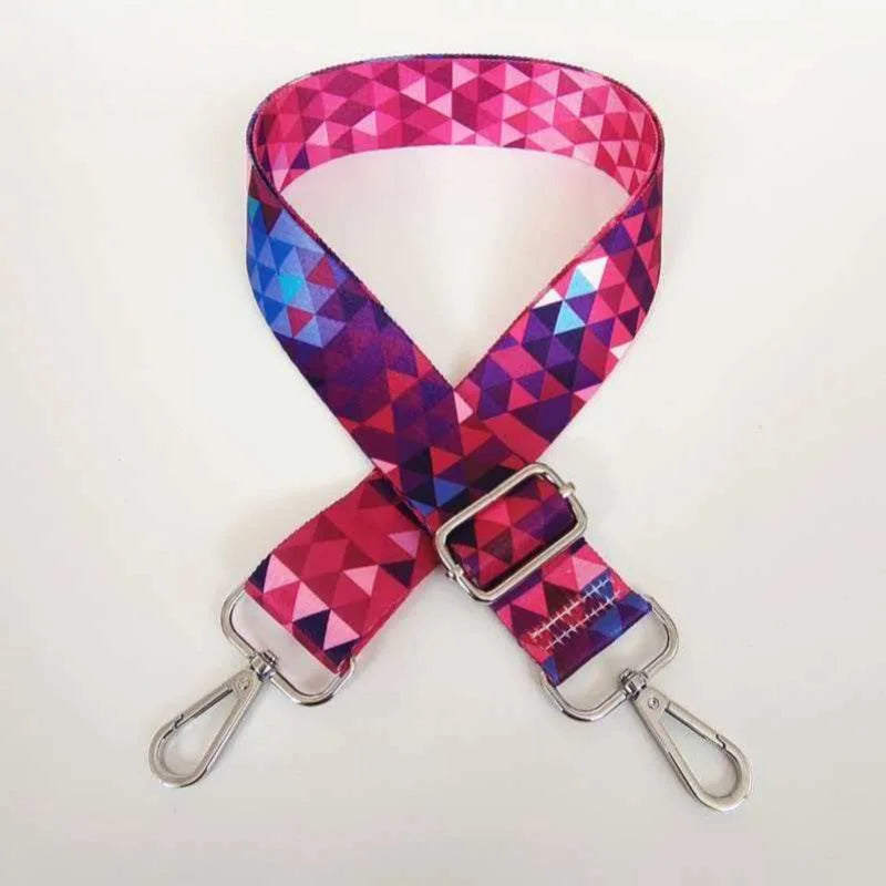 A magenta and purple geometric patterned fabric strap for an adjustable crossbody bag.