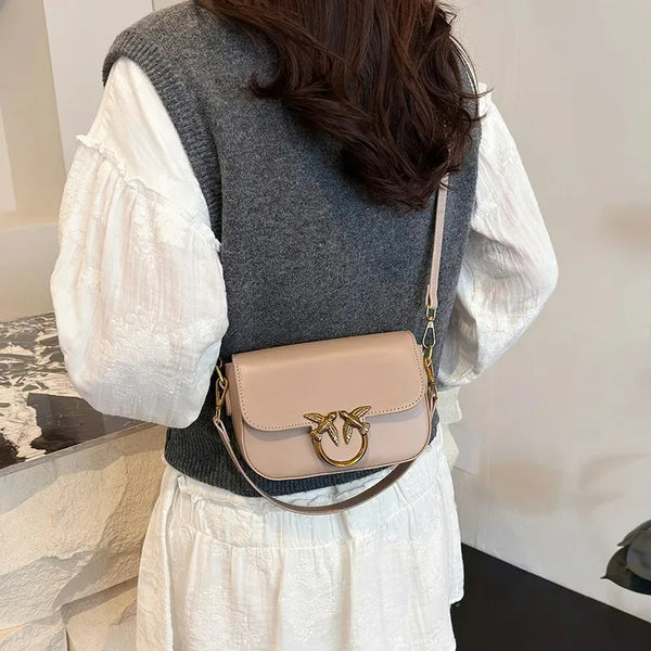 Una mujer lleva un bolso cruz cuadrado rosa claro minimalista sobre una blusa blanca y un suéter gris.