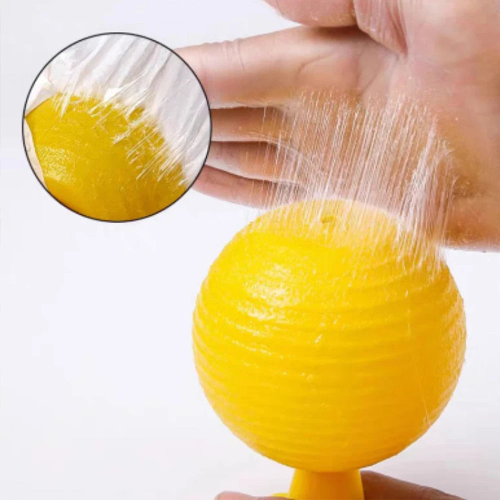 A hand is squeezing a yellow sticky fruit fly trap ball, showing the sticky substance being released.