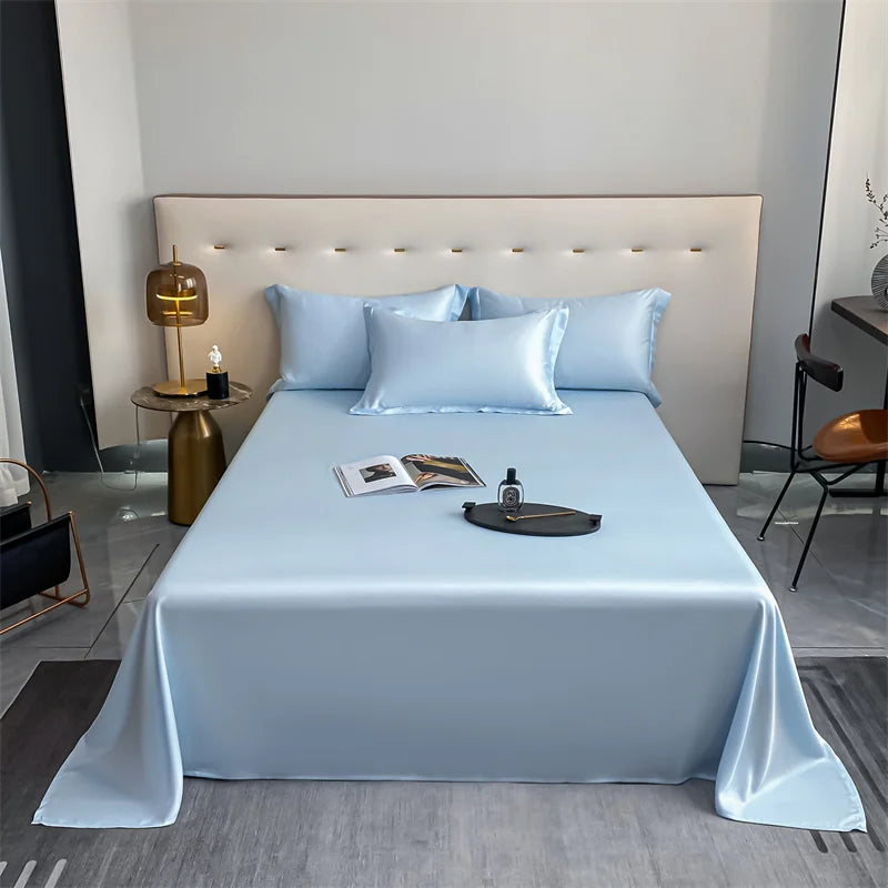 A bed dressed with a light blue luxury bamboo flat sheet and white pillows against a neutral wall.