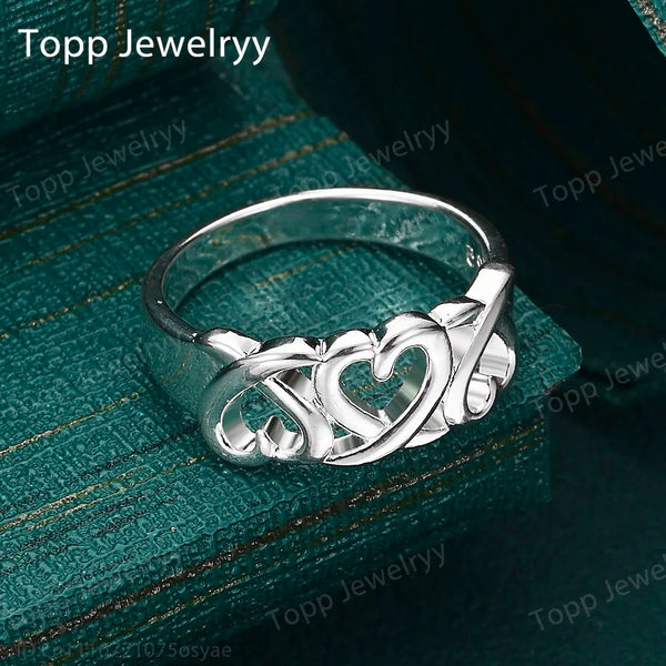 Bague en forme de cœur creux argenté présentée sur un velours vert foncé.