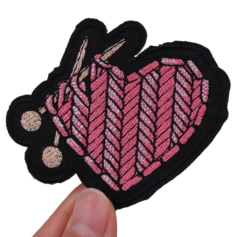 A set of black embroidered iron-on patches shaped like hearts with pink and beige stitching.