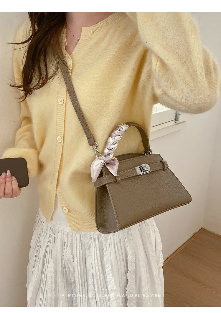 Eine Frau trägt einen gelben Strickpullover und einen weißen Rock und hält eine elegante braune Kunstleder-Clutch.