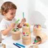 A toddler is sorting colored wooden sticks into a wooden container, demonstrating fine motor skills.