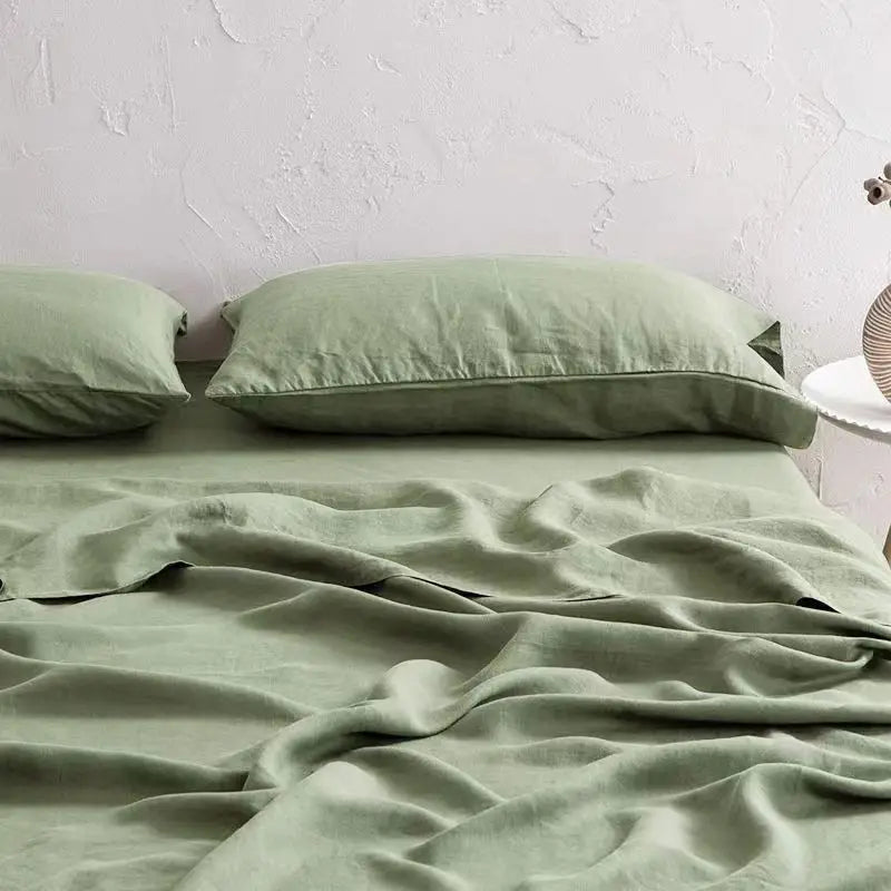 A light sage green linen bed sheet set with matching pillows draped on a bed.