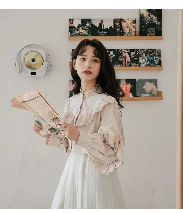 A woman wearing a cream vintage lace long sleeve blouse and white skirt, standing in front of a wall display.