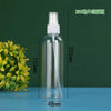 A clear glass spray bottle with a white pump dispenser is shown next to a green plant on a blue surface.