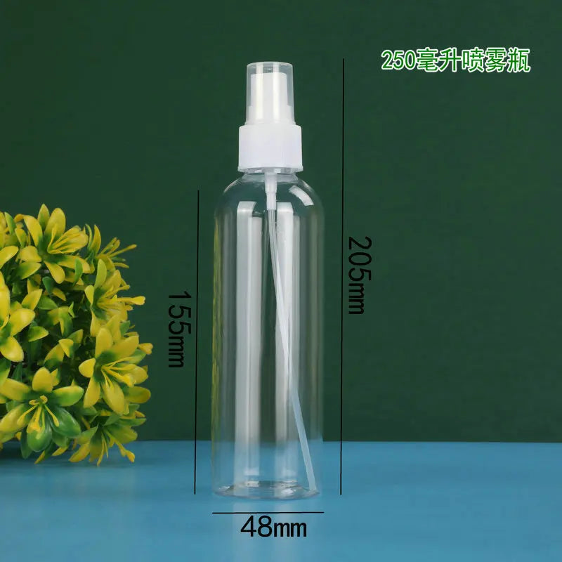 A clear glass spray bottle with a white pump dispenser is shown next to a green plant on a blue surface.