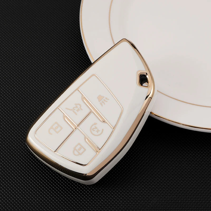 A white durable TPU car key fob cover with a gold rim and various buttons is shown resting on a dark surface.