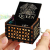 A dark wooden music box with an engraved queen design is held in a hand.