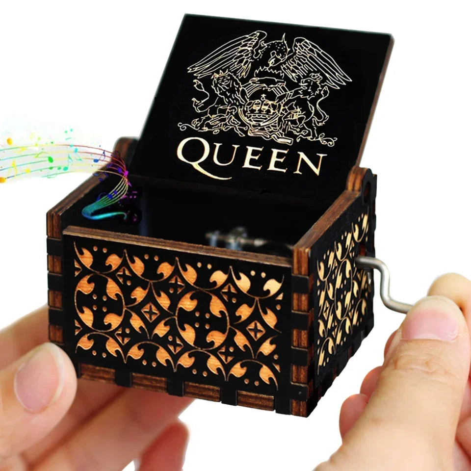A dark wooden music box with an engraved queen design is held in a hand.