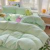 A light mint green cotton bedding set featuring a duvet cover, flat sheet, and pillowcases with a yellow stuffed toy.