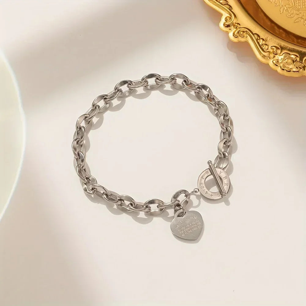 A silver stainless steel chain bracelet with a double heart pendant resting on a light surface.