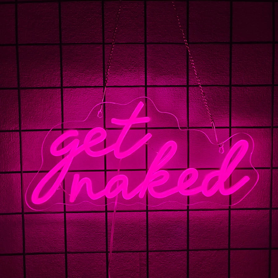 A neon sign shaped like the words get naked is illuminated in bright pink on a dark grid background.