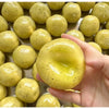 A hand holds a yellow potato slushie squishy toy with a textured surface against a background of similar toys.