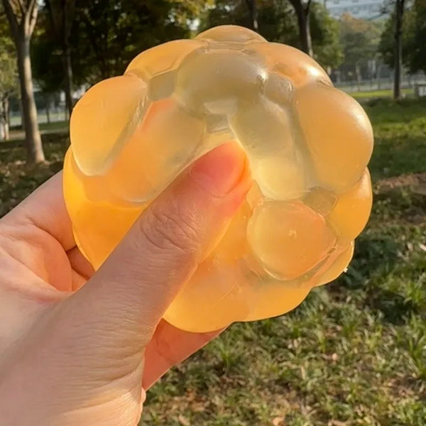 Une main tient un cube anti-stress jaune translucide aux formes arrondies et bullées, à l'extérieur.