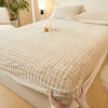 A beige faux fur fitted sheet is being held, displayed on a bed with white linens and natural light.
