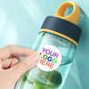 A hand holds a clear water bottle with a yellow cap and a dark blue silicone seal, featuring green leaves inside.