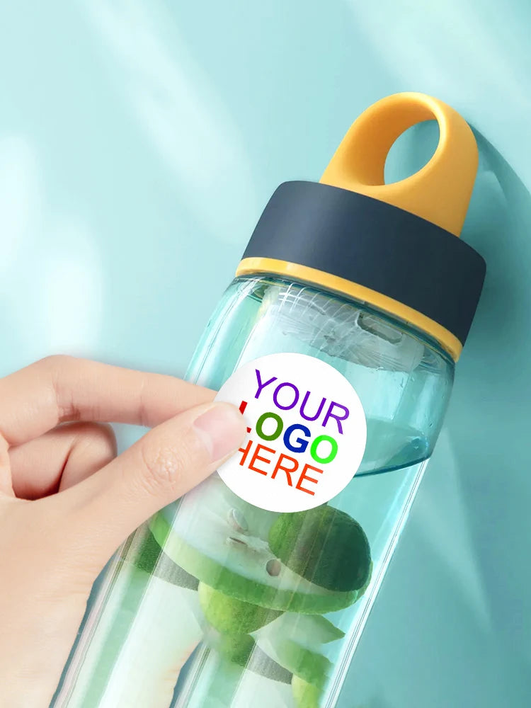 A hand holds a clear water bottle with a yellow cap and a dark blue silicone seal, featuring green leaves inside.