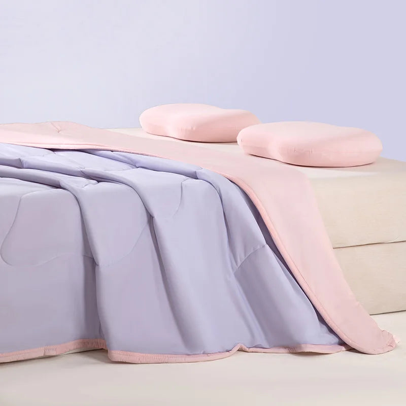 A light pink ice silk cooling blanket is draped over a beige surface with soft pink pillows.