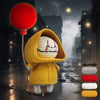 A crocheted yellow animal figure wearing a hood and holding a red lantern in a dark, misty street setting.