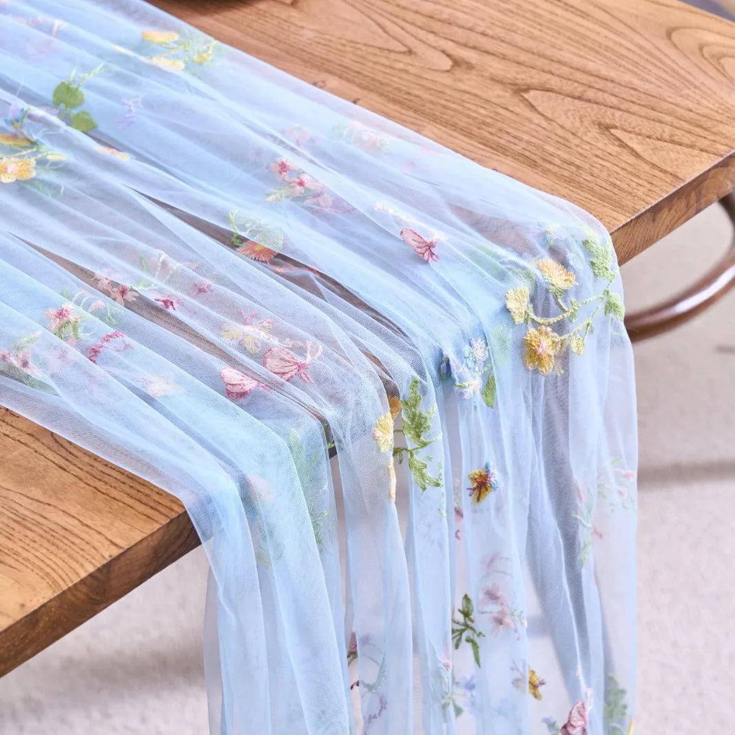 Light blue tulle table runner featuring delicate floral embroidery on a wooden table.