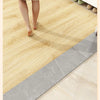 A close-up view of a light wood grain floor sticker being applied to a surface, showing the peel-and-stick texture.