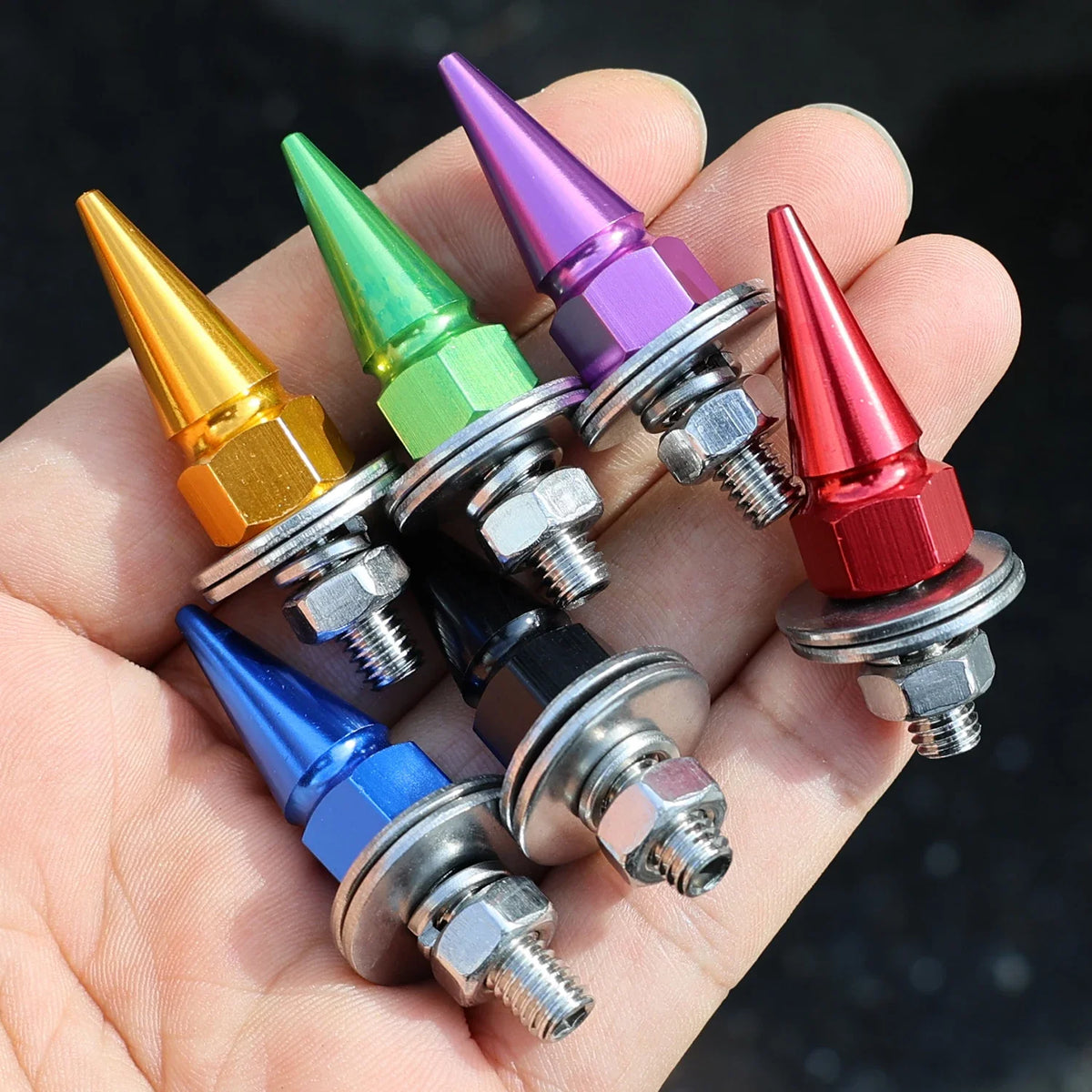 A hand holds a set of colorful rust-resistant license plate screws with conical heads and threaded bases.