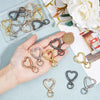A hand holds various heart-shaped spring hook keychains in gold and silver tones, displayed next to a coin.