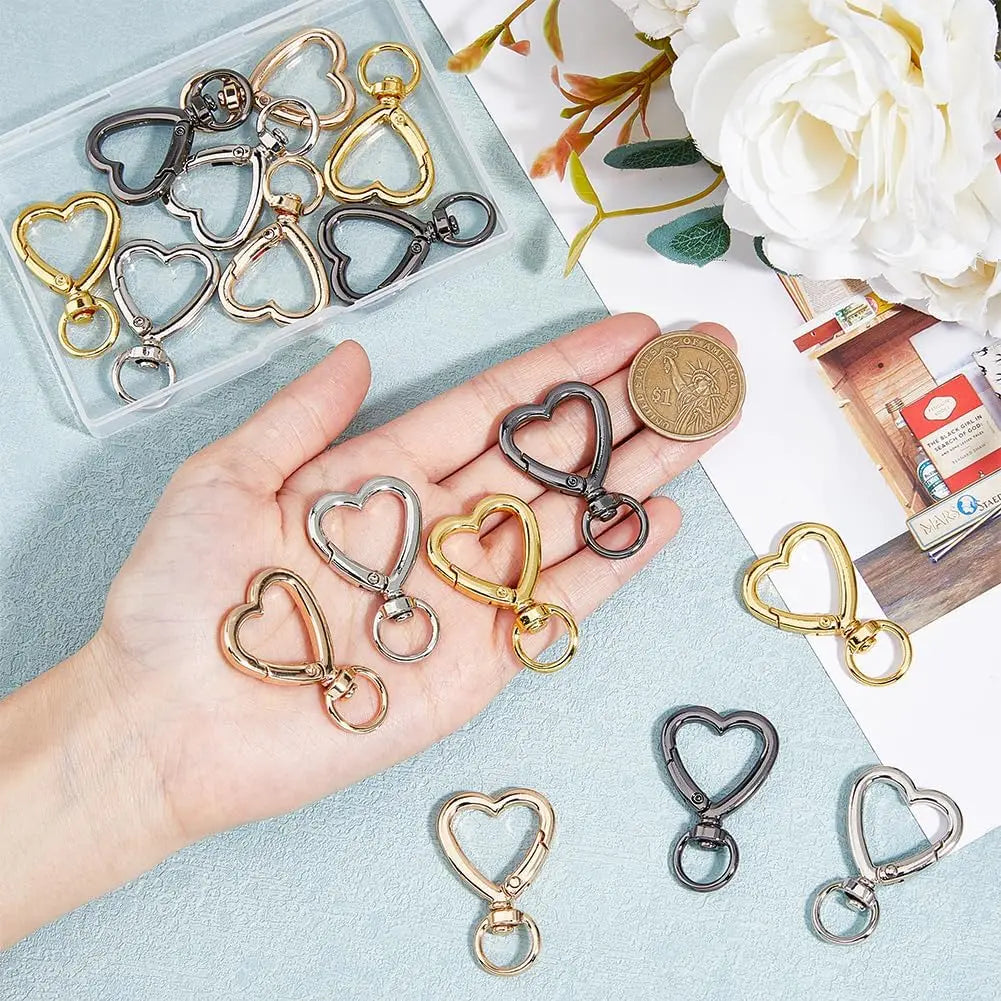 A hand holds various heart-shaped spring hook keychains in gold and silver tones, displayed next to a coin.