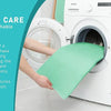 A hand places a green reusable waterproof underpad into the drum of a white washing machine.