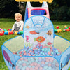 A blue and pink foldable ball pit with a basketball hoop is set up outdoors on green grass.