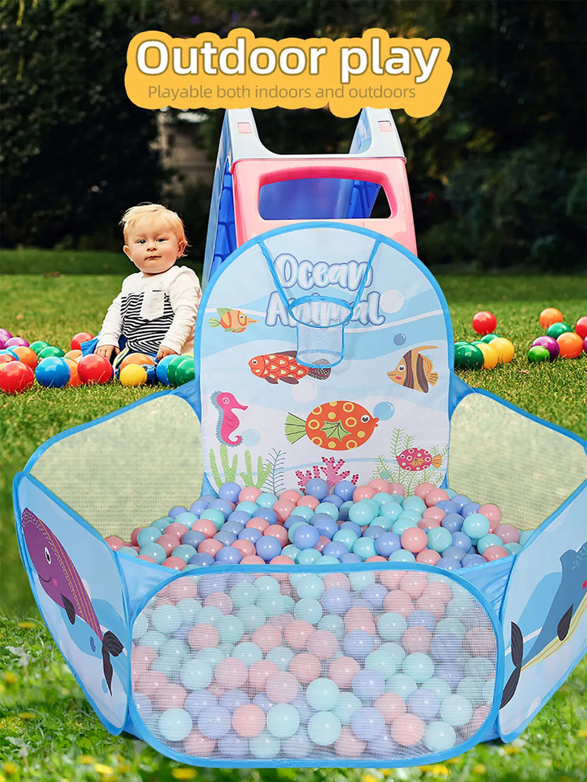 A blue and pink foldable ball pit with a basketball hoop is set up outdoors on green grass.