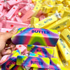 A hand holds a squishy butter fidget toy in various colors, including purple and yellow.