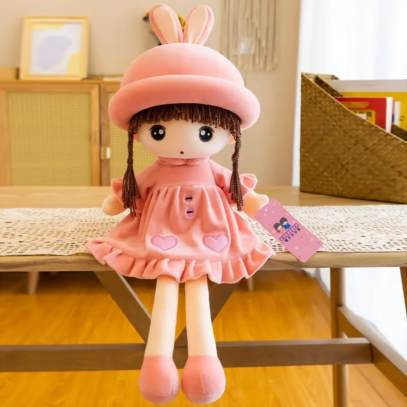 A pink rabbit fairy plush doll with large ears and a dress sitting on a wooden table.