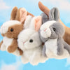 A hand is holding three soft plush bunny toys: brown, white, and gray.