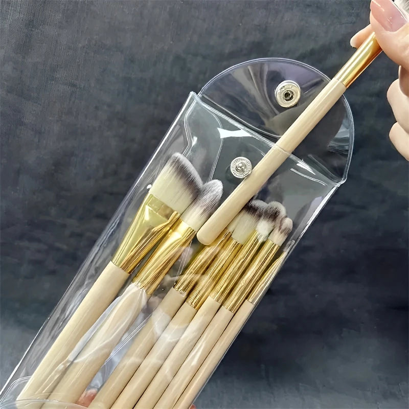 A transparent PVC cosmetic bag holds several makeup brushes with gold ferrules and wooden handles.