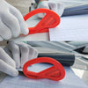 A hand wearing a white glove is using an orange vinyl wrap application tool on a sheet of graph paper.