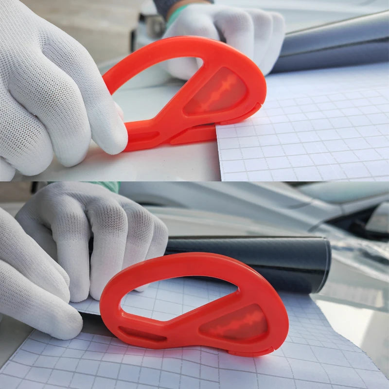 A hand wearing a white glove is using an orange vinyl wrap application tool on a sheet of graph paper.
