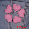 A set of five pink glitter heart iron-on embroidered patches placed on a denim fabric.