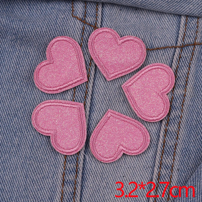 A set of five pink glitter heart iron-on embroidered patches placed on a denim fabric.
