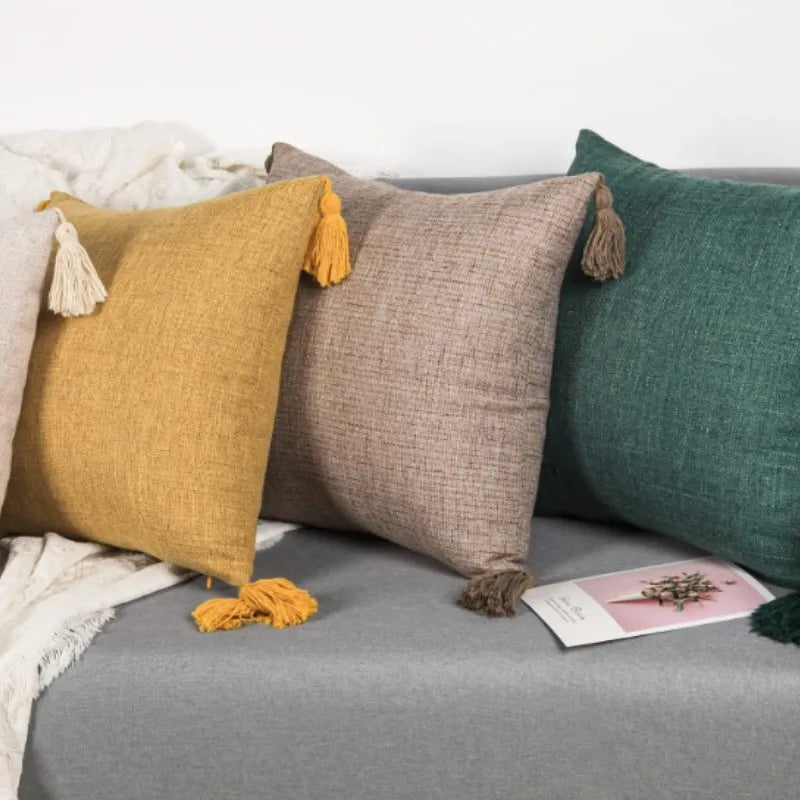 A collection of linen throw pillows in mustard yellow, beige, and deep green with tasseled edges on a gray surface.