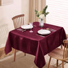 A deep burgundy satin tablecloth is set for dining with white plates and silverware, featuring a floral centerpiece.