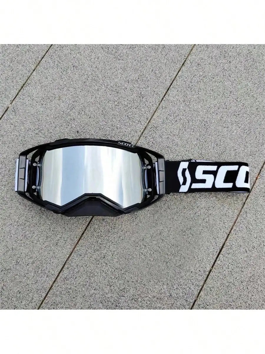 A pair of black SCOTT motocross goggles resting on a gray concrete surface.