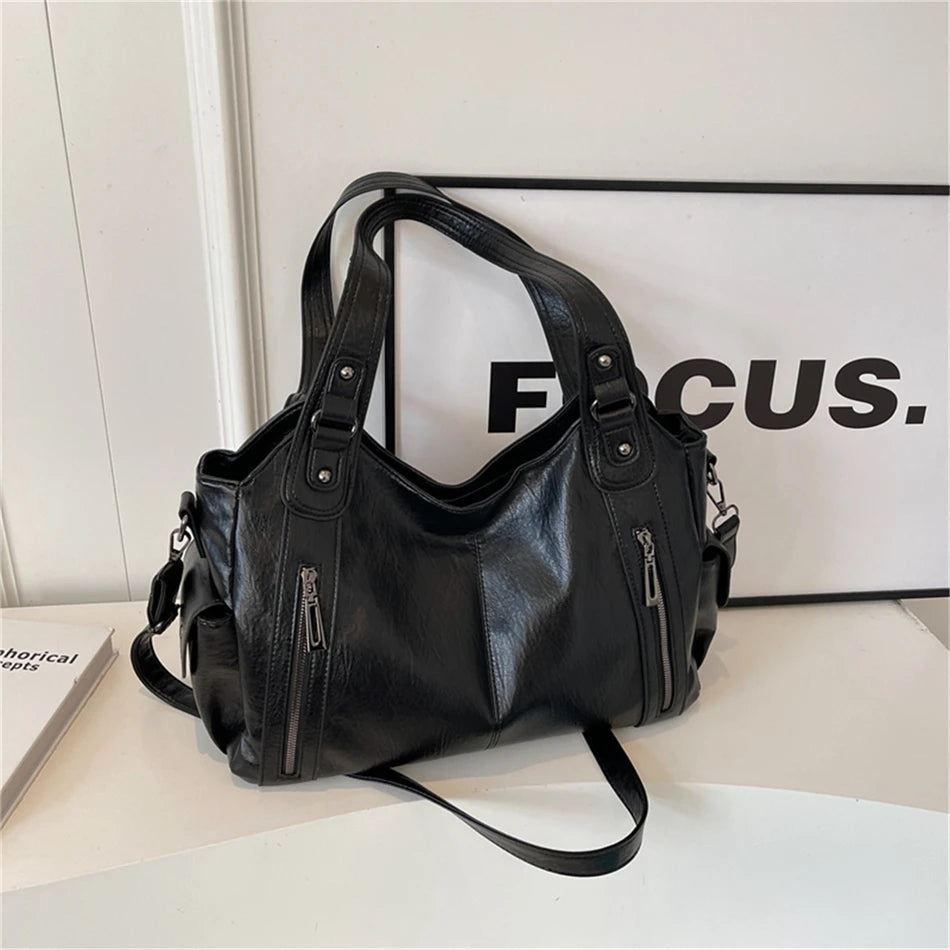 A black vintage leather tote bag with multiple pockets is displayed on a white surface next to a framed sign.