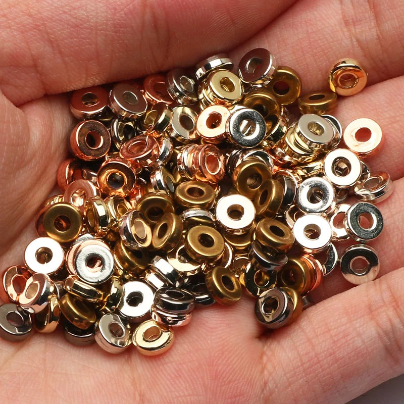 A handful of round acrylic spacer beads in various gold and silver tones held in a person's hand.
