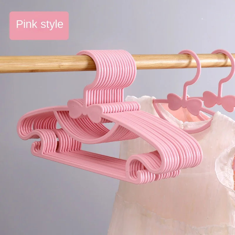Pink plastic hangers with bow designs hanging from a wooden rod.
