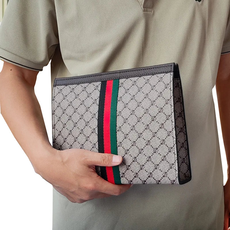 A men's designer clutch bag with a gray and black monogram pattern and red and green stripes is held by a person wearing a kh