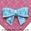 A light blue sequin bow made of fabric is shown on a pink background.