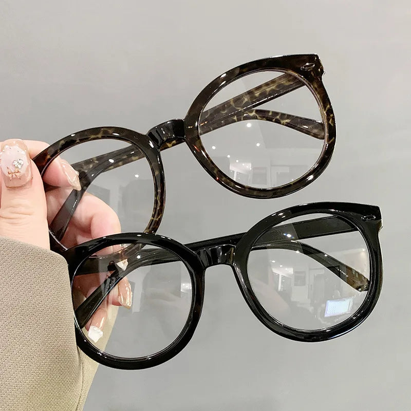 Eine Hand hält eine große Schildpatt-Brille mit dunklem Rahmen und klaren Gläsern.